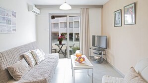 En moderne stue med sofa, sofabord med frugt, fjernsyn og en balkon med udsigt.