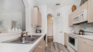 Een moderne keuken met een groot eiland, een RVS spoelbak, witte kastjes en een magnetron.