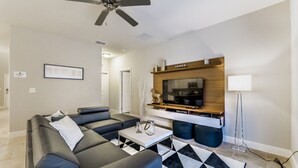 A modern living room with a sectional sofa, a coffee table, a TV mounted on a wooden wall, and a ceiling fan. - Luxury Villa With Private Pool on Solterra Resort, Orlando Villa 4946 (Davenport)
