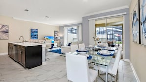 A spacious dining area with a glass table, white chairs, and a modern kitchen with dark cabinetry. - Imagine You and Your Family Renting This 5 Star Villa on Storey Lake Resort , Orlando Townhome 5519 (Kissimmee)