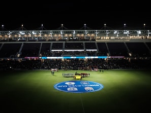 Een stadion met een groot, verlichte uitslagenbord en een rond logo op het veld.