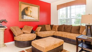 A living room with a red wall, a large sectional sofa, a coffee table, and a painting of a lion. - Luxury 6 Bedroom Villa on Emerald Island Resort, Orlando Villa 1460 (Kissimmee)