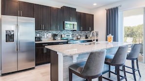 A modern kitchen with dark cabinets, stainless steel appliances, a granite countertop, and a bar area with bar stools. - Luxury Villa With Private Pool on Encore Resort at Reunion, Orlando Villa 4695 (Kissimmee)