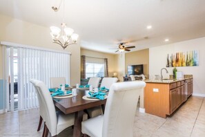 A dining area with a wooden table and white chairs, a kitchen with a wooden island, and a ceiling fan. - Luxury 4 Bedroom Townhome on Storey Lake Resort, Orlando Townhome 2718 (Kissimmee)