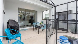 Eine Terrasse mit Tisch und Stühlen, ein überdachter Sitzbereich und Blick ins Innere durch Glastüren.