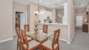 A dining area with a glass-top table and wooden chairs, a kitchen with white cabinets, and a hallway with a door. - Luxury Home on Bahama Bay Resort,minutes From Disney World, Orlando Condo 5057 (Davenport)