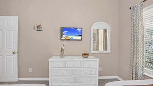 A bedroom with a white dresser, a television mounted on the wall, a mirror, and a door. - Luxury Home on Bahama Bay Resort,minutes From Disney World, Orlando Condo 5057 (Davenport)