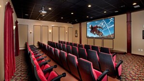 Un teatro con hileras de asientos rojos y negros, una pantalla grande mostrando a un astronauta y una alfombra estampada.