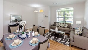 A dining area with a table set for four, a sofa, a coffee table, and a large window providing natural light. - Luxury 5 Bed Villa, Perfect for Large Groups, 1005 (Davenport)