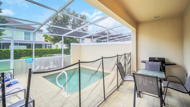 Un espace extérieur abrité avec une piscine, une structure en verre, une table de billard et une chaise.