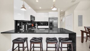 Une cuisine moderne dotée d’un grand îlot central, d’appareils électroménagers en acier inoxydable et de luminaires suspendus.