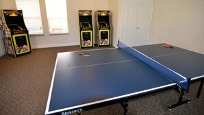 Une table de ping-pong ornée du logo Brunswick, deux bornes d’arcade et une porte dans une pièce dont le sol est recouvert de moquette.