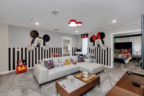 A modern living room with a sectional sofa, a coffee table, and a wall with Mickey Mouse decorations. - Imagine Your Family Renting This Amazing Mansion on Storey Lake Resort With the Best 5 Star Amenities, Orlando Mansion 3677 (Kissimmee)