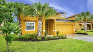 Une maison jaune avec un garage, entourée de pelouses bien entretenues et de palmiers.
