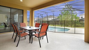 Un espace patio avec une table et des chaises en verre, une piscine et une vue sur les maisons et les arbres.