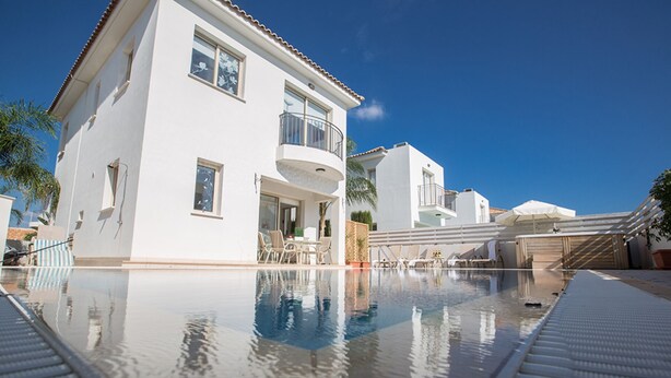 Een modern resort met een groot zwembad, terraszitplaatsen en een helderblauwe lucht.