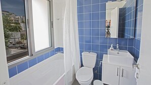 Een badkamer met een badkuip, toilet en wastafel, met blauwe tegels en een raam.