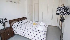 Een slaapkamer met een bed, nachtkastje, airconditioning, kledingkast en lamp.