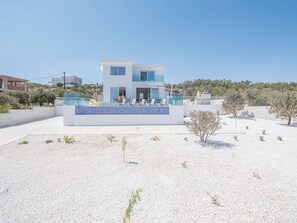 A modern two-story house with a balcony, surrounded by a white gravel area and sparse vegetation. - Luxury 4 Bedroom Villa With Private Pool, Protaras Villa 1222 (Paralimni)