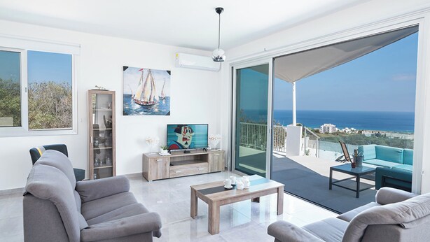 A modern living room with a large sliding glass door leading to a balcony with a sea view. - Luxury 4 Bedroom Villa With Private Pool, Protaras Villa 1222 (Paralimni)