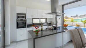 A modern kitchen with white cabinets, a central island, and a view of a swimming pool. - Luxury Modern 3 Bed Villas Near the Beach, Protaras Villa 1077 (Paralimni)