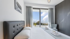 A modern hotel room with a large bed, a grey upholstered headboard, a grey wardrobe, and a view of the outdoors through a glass door. - Luxury Modern 3 Bed Villas Near the Beach, Protaras Villa 1077 (Paralimni)
