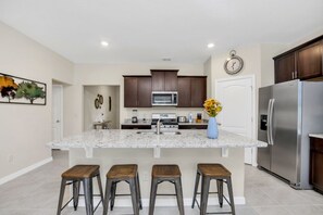 A modern kitchen with a central island, stainless steel appliances, and wooden stools.