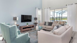 A living room with a TV, two armchairs, a sofa, and a glass coffee table. - Perfect 5 Bedroom Villa on Storey Lake Resort, Orlando Villa 4900 (Kissimmee)