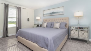 A bedroom with a large bed, two bedside tables, a window with curtains, and a painting on the wall. - Perfect 5 Bedroom Villa on Storey Lake Resort, Orlando Villa 4900 (Kissimmee)