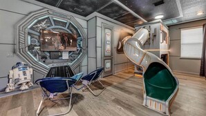 A room with a Star Wars theme, including a large window with a view of space, a slide, and two R2-D2 figures.