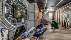A room with a large screen displaying a movie scene, a Star Wars-themed wall, and a unique chair design.