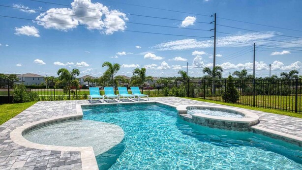 A swimming pool with a hot tub, surrounded by a paved deck and lounge chairs.