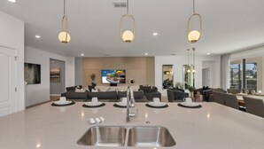 Une cuisine moderne dotée d’un îlot central, d’un évier en acier inoxydable et de luminaires suspendus.