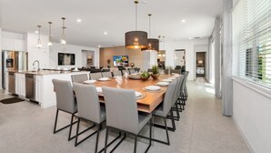 Une cuisine moderne dotée d’un îlot central, d’un coin repas avec une longue table et d’une vue sur l’extérieur grâce à de grandes fenêtres.