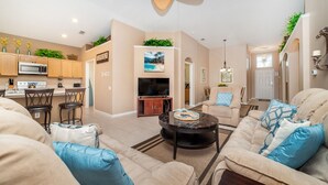 A modern living room with a fireplace, a dining area with bar stools, and a kitchen with wooden cabinets and a microwave. - Luxury Villa on Windsor Palms Resort With a Private Pool, Orlando Villa 4878 (Kissimmee)