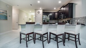 Une cuisine moderne avec des meubles de couleur sombre, un plan de travail en marbre et quatre tabourets de bar blancs.