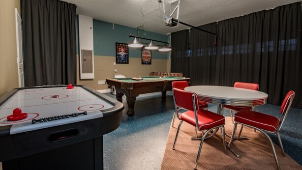 Une pièce équipée d’une table de billard, d’un baby-foot et d’une table de jeu de flipper. On y trouve des chaises rouges disposées autour d’une petite table.
