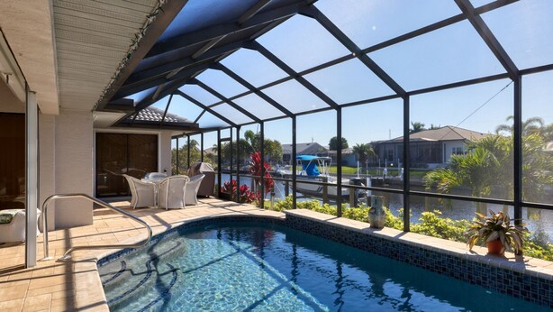 Ein Schwimmbad mit Glasveranda, eine Terrasse mit Stühlen und Blick auf eine Marina.