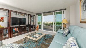 Un salon moderne avec un téléviseur, des étagères, un canapé et un balcon offrant une vue agréable.