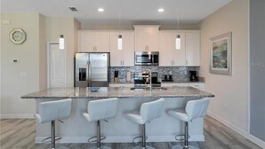 Una cocina moderna con una isla central, electrodomésticos de acero inoxidable y taburetes blancos.