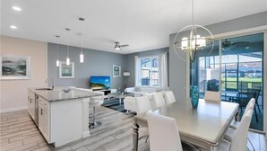 Una cocina moderna con una isla central, muebles blancos y un comedor con una mesa grande y sillas.