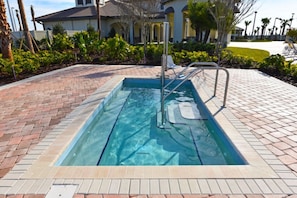 Una piscina rectangular con una escalera metálica, rodeada por un borde de ladrillo y un camino pavimentado.