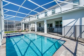 Una piscina con piso de vidrio, rodeada por un patio cubierto con sillas y una cerca.