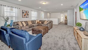 A spacious living room with a sectional sofa, a blue armchair, and a wooden entertainment center. - Enjoy a Holiday of a Lifetime in a Luxury Villa on Windsor at Westside Resort, Orlando Villa 5051 (Kissimmee)
