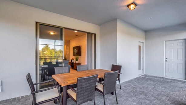 A patio with a wooden table and wicker chairs, a sliding glass door leading to an interior space, and a door to the right. - Enjoy a Holiday of a Lifetime in a Luxury Villa on Windsor at Westside Resort, Orlando Villa 5051 (Kissimmee)