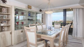 A dining area with a glass table and chairs, a chandelier, and a view of the city through large windows. - Perfect Apartment on The Anchorage, Siesta Key Apartment 1022 (Siesta Key)