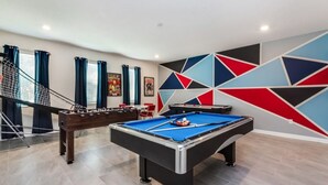A pool table in a room with a geometric wall design, a foosball table, and a staircase with blue curtains. - Rent a Luxury Mansion on Storey Lake Resort, Minutes From Disney, Orlando Mansion 3232 (Kissimmee)