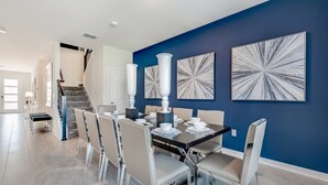 A dining area with a dark table, white chairs, and blue walls with abstract art. - Rent a Luxury Mansion on Storey Lake Resort, Minutes From Disney, Orlando Mansion 3232 (Kissimmee)