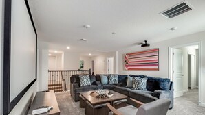 A modern living room with a sectional sofa, a coffee table, and a TV. There is a staircase leading to another level, and a door to the right. - Rent a Luxury Mansion on Storey Lake Resort, Minutes From Disney, Orlando Mansion 3232 (Kissimmee)