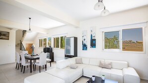 A spacious living room with a large white sofa, a dining area with a table and chairs, and artwork on the walls. - Rent a Luxury Villa in Cyprus Close to the Beach, Protaras Villa 1220 (Paralimni)